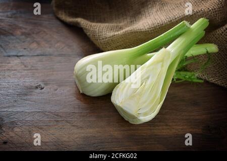 Halbierte rohe Fenchelbirne auf einem dunklen rustikalen Holztisch, gesundes mediterranes Gemüse, Kopierraum, ausgewählter Fokus, enge Schärfentiefe Stockfoto