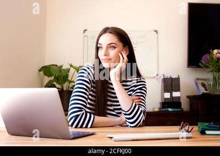 Aufnahme einer schönen jungen Frau, die am Schreibtisch hinter ihrem Computer sitzt und von zu Hause aus auf die Witwe schaut. Stockfoto