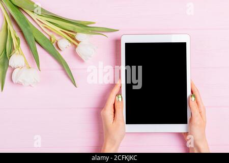 Persönlicher Tablet-pc mit leerem Touchscreen neben Blumenstrauß Zarte Tulpenblüten auf rosafarbenem Holztisch Stockfoto