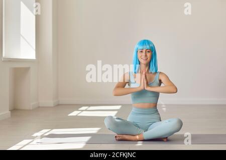 Junge Frau sitzt in einer leichten Pose auf einer Yogamatte Gym tun Namaste Geste und Blick auf die Kamera Stockfoto