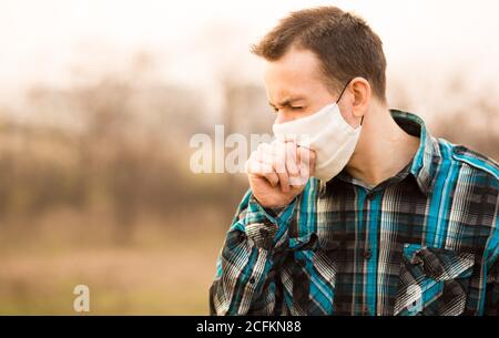 Grippe, Erkältungskonzept. Porträt des jungen Mannes krank fühlen, Husten, Gesichtsmaske tragen im Freien Stockfoto