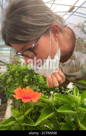 Covid-19. Frau trägt schützende Gesichtsmaske riechende Pflanzen. Nahaufnahme Stockfoto