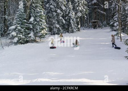 Russland, das Plateau Lago-Naki, Adygeya Republik - Januar 28.2017: Kinder und Erwachsene fahren auf Schlitten auf Schneehügeln zum Skifahren. Sonniger Wintertag im Mo Stockfoto