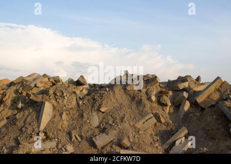 Ein großer Haufen von Felsen, Betonblöcken und Sand gegen den blauen Himmel. Bauabfälle, Betonreste aus dem Abriss, Straße. Stockfoto