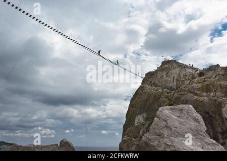 Simeiz, Jalta, Krim, Russland-09. September 2018: Mutige Menschen gehen auf einer Seilbrücke zwischen dem Felsen Diva und dem Ufer hoch in den Wolken. Beliebte E- Stockfoto