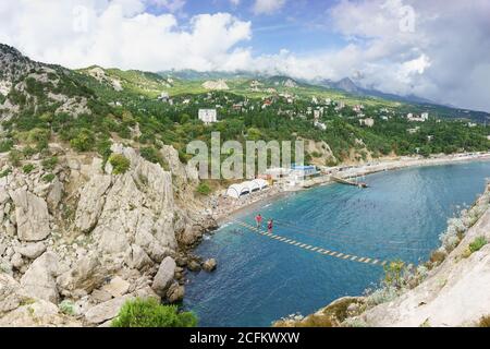 Simeiz, Jalta, Krim, Russland-09. September 2018: Draufsicht auf das Dorf und Touristen zu Fuß auf einer Scharnierseilbrücke zwischen dem Ro gestreckt Stockfoto