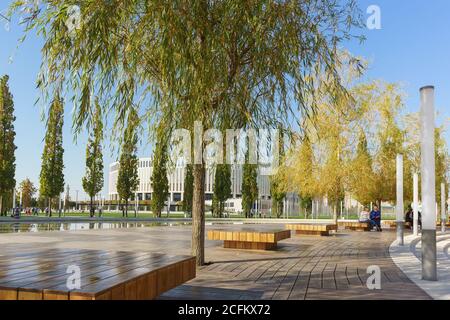 Krasnodar, Russland-19. Oktober 2018: Holzbänke unter den Weiden auf der Terrasse in der Nähe des halbrunden Teich der neuen Stadt Park Krasnodar in der Nähe der Stockfoto