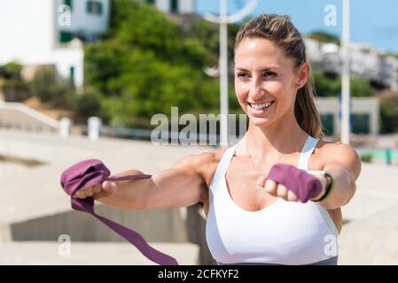 Starke weibliche tun Ausfallschritte mit Gummiband während des Trainings in der Nähe Meer an sonnigen Tag weg schauen Stockfoto