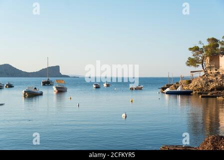 Malerische Landschaft der alten Bucht in der Nähe des Meeres mit festverankerten Booten Auf felsigen Ufer und Bäumen unter blauem Himmel in Sa Caleta Stockfoto