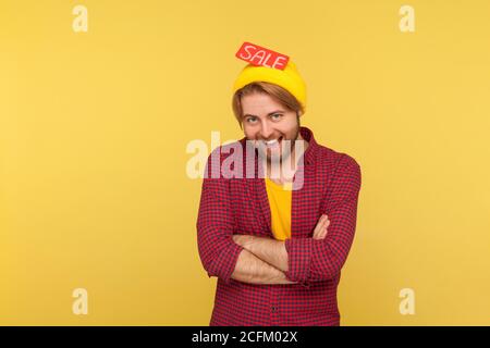 Fröhlicher trendy Hipster Kerl stehen mit Sale Wort in seiner Mütze Hut, Blick auf die Kamera mit toothy Lächeln, Freude Rabatte, Black Friday niedrigen Preisen Stockfoto