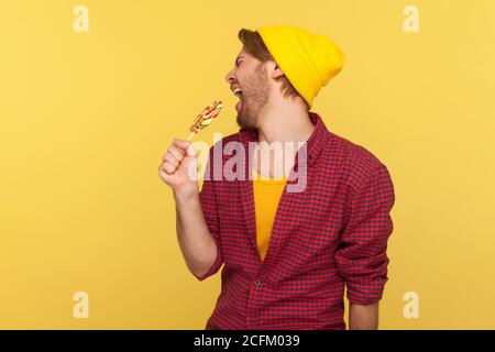 Erstaunlich sorglos Hipster Kerl in Beanie Hut, karierte Hemd schreien in Lollipop wie Mikrofon, singen laut als Popstar in Karaoke, Spaß haben. Stockfoto
