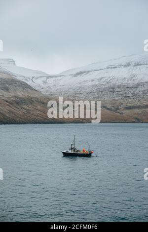 Fischboot auf dem Meer in der Nähe schneebedeckten Bergkette während Winter auf der färöer Insel Stockfoto