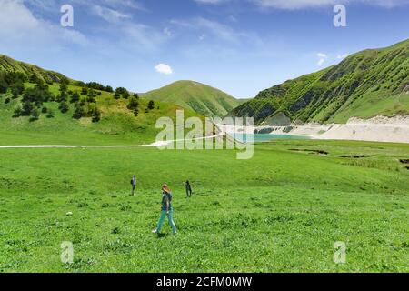 Botlikh Bezirk, Dagestan, Russland - 01. Juni 2019: Junge Menschen steigen zum See Kezenoi am. Grünes Gras auf den Berghängen im Frühsommer Stockfoto