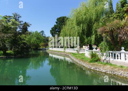 Park Yuzhnye Kultury, Adler, Sotschi, Russland - 05. Mai 2019: Menschen gehen um den Teich im alten Park. Der Teich ist mit einer weißen Balustrade eingezäunt Stockfoto