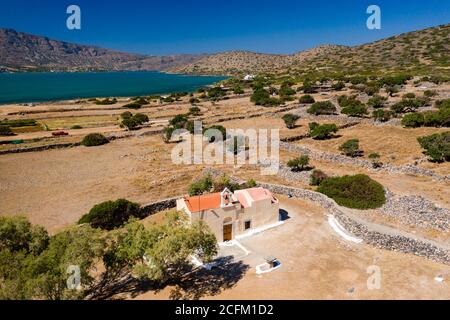 Luftaufnahme einer kleinen Kirche neben einem blauen Meer auf einer heißen griechischen Insel (Ascension Church, Elounda, Kreta) Stockfoto