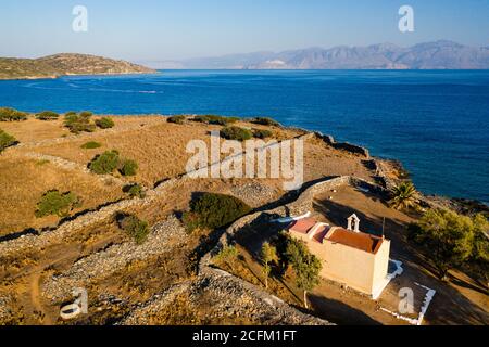 Luftaufnahme einer kleinen Kirche neben einem blauen Meer auf einer heißen griechischen Insel (Ascension Church, Elounda, Kreta) Stockfoto