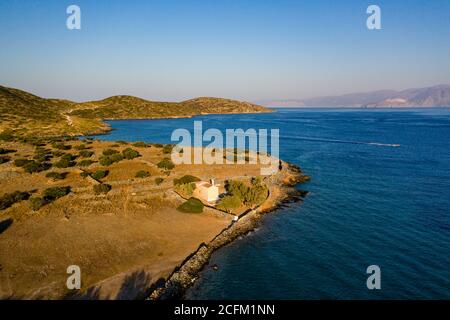 Luftaufnahme einer kleinen Kirche neben einem blauen Meer auf einer heißen griechischen Insel (Ascension Church, Elounda, Kreta) Stockfoto