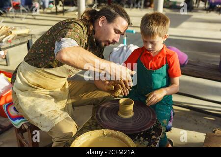 Moldawisch, Krymsk, Russland-05. Oktober 2019: Meister lehrt Jungen Keramik aus Ton zu machen. Rotierendes Töpferrad. Selektiver Fokus auf Hände Stockfoto