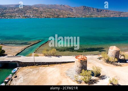 Alte Windmühlen und Kanal auf einem schmalen Damm und Stätte einer antiken minoischen Stadt (Elounda, Kreta, Griechenland) Stockfoto