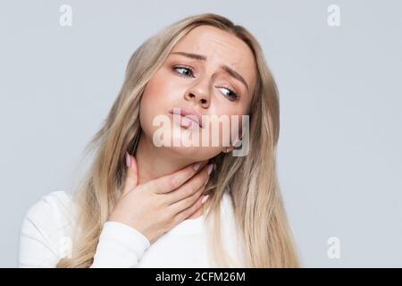 Nahaufnahme Porträt der kranken jungen blonden Frau mit Halsschmerzen, die Hand an ihrem Hals. Halsschmerzen, schmerzhaftes Schlucken. Entzündung der oberen r Stockfoto