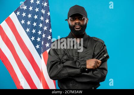 Junge bärtige Sicherheit der afrikanischen Ethnie in schwarzer Uniform Kreuzung Seine Arme Stockfoto