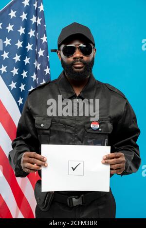 Afrikanischer Sicherheitsdienst in schwarzer Uniform und Sonnenbrille mit Stimmzettel Papier Stockfoto