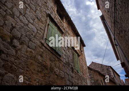 Alte, abgenutzte, grün gefärbte Fensterläden aus Holz auf dem Steinhaus, traditionell in der dalmatinischen Region von Kroatien Stockfoto