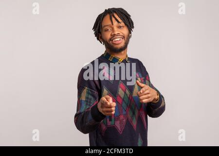 Hey, du! Zufrieden schöner Kerl mit Dreadlocks zeigen Finger auf Kamera und Blick mit toothy Lächeln, flirten, bewundern. Innenaufnahme des Studios isola Stockfoto