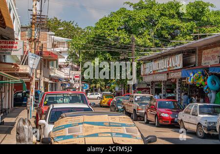 Acapulco, Mexiko - 25. November 2008: Alte Innenstadt. Geschäftsstraße mit geparkten Autos und Fußgängern. Geschäfte mit offenem Fenster, viele Schilder und Grünflächen Stockfoto