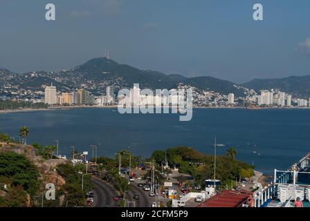 Acapulco, Mexiko - 25. November 2008: Die blaue Wasserbucht mit Strand- und Hochhäusern entlang der Küste. Hintergrund von grünen Hügeln mit Häusern beladen Stockfoto