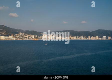 Acapulco, Mexiko - 25. November 2008: Die blaue Wasserbucht mit Strand- und Hochhäusern entlang der Küste. Hintergrund von grünen Hügeln mit Häusern beladen Stockfoto