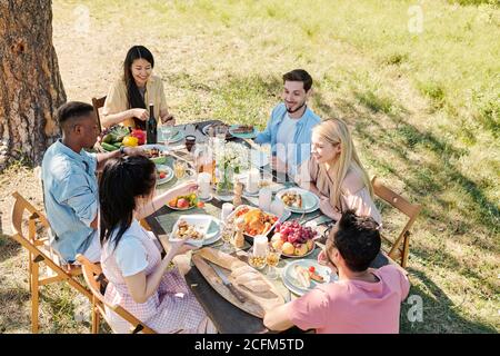 Gruppe von jungen glücklichen Freunden am Tisch mit serviert versammelt Hausgemachtes Essen Stockfoto