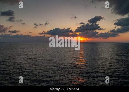 Acapulco, Mexiko - 25. November 2008: Orangefarbener Sonnenuntergang taucht ins dunkle Wasser Pazifischer Ozean unter dunkler Wolkenlandschaft gegen beige-grauen Himmel. Stockfoto