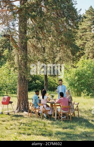 Junger Mann, der vor seinem Tisch stand Freunde beim Abendessen im Freien Stockfoto