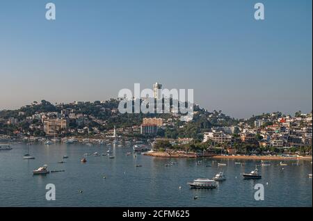 Acapulco, Mexiko - 25. November 2008: Pharos von Santa Lucia hinter Jachthafen mit Hügel und hohen Gebäude hinten unter Dämmerungshimmel. Blue Bay Water Stockfoto