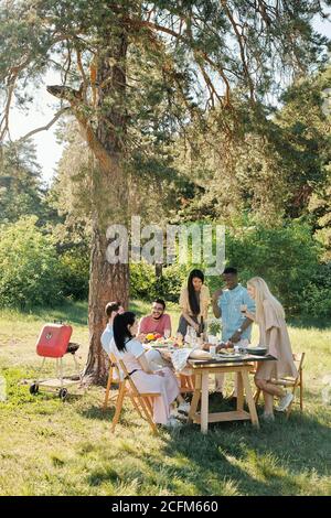 Drei junge interkulturelle Menschen stehen an Tisch und haben Essen Stockfoto