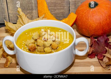 Herbst-Kürbissuppe mit Sesam auf Holzgrund. Kürbispüree-Suppe mit Crackern und Sesamsamen auf dem Hintergrund herbstlicher Blätter Stockfoto