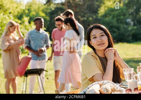 Junge Frau von asiatischer Ethnie sitzt von Tisch serviert in Vorderseite der Kamera Stockfoto
