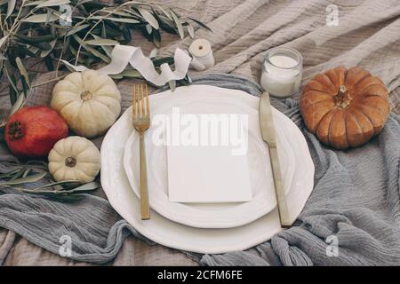 Herbsttisch mit goldenem Besteck, Olivenzweigen und Porzellanteller. Kürbisse und Granatapfelfrüchte. Leeres Menü-Karten-Mockup. Fallen Stockfoto