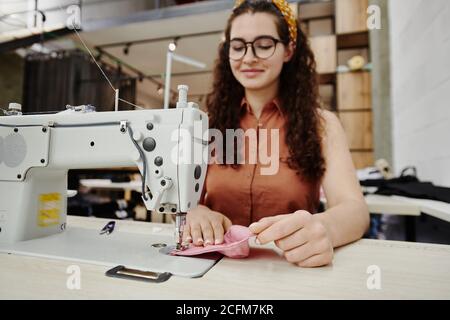 Hände der glücklichen jungen Näherin durch elektrische Nähmaschine machen Schulterpolster Stockfoto