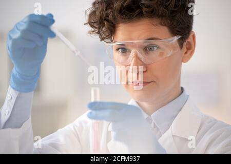 Laborangestielter in Brillen, die Flüssigkeit von der Pipette in die Brille Tropfen Kolben Stockfoto