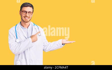 Hübscher junger Mann mit Bär trägt Doktor Uniform erstaunt und lächelt an der Kamera, während mit der Hand und zeigt mit Finger. Stockfoto