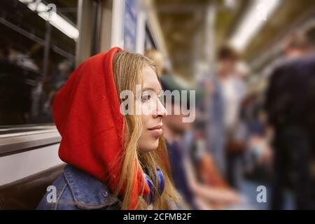 Junge Frau im roten Hoodie im Auto des Zuges in der U-Bahn zur Hauptverkehrszeit. Passagiere im Fahrgastraum eines Elektrozuges. Stockfoto