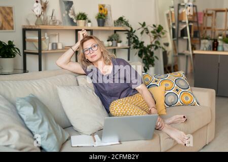 Reife blonde entspannte Geschäftsfrau in Casualwear sitzen auf der Couch Zu Hause Stockfoto