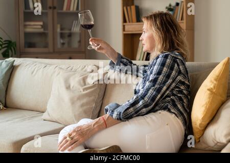 Ernst blonde reife Frau in Casualwear Blick auf Glas Rotwein Stockfoto