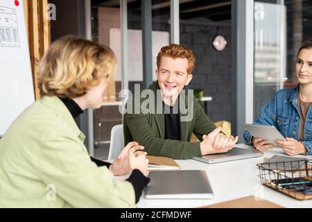 Glückliche junge Entwickler von mobilen Anwendungen im Gespräch mit einer Frau Kollegen Stockfoto