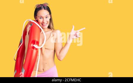 Schöne Brünette junge Frau trägt Bikini und hält Lebensretter schweben Lächelnd glücklich zeigt mit Hand und Finger zur Seite Stockfoto