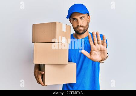 Schöner Mann mit Bart tragen Kurier Uniform halten Lieferpakete tun aufhören zu singen mit Handfläche der Hand. Warnung Ausdruck mit negativen und Stockfoto