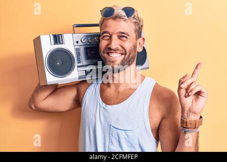 Junger, schöner blonder Mann mit Bart, der eine Sonnenbrille trägt Musik mit Boombox lächelnd glücklich zeigen mit Hand und Finger Zur Seite Stockfoto