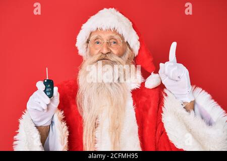 Alter älterer Mann mit grauen Haaren und langem Bart tragen santa claus Kostüm mit Autoschlüssel lächelnd mit einer Idee Oder Frage zeigt Finger mit glücklich Stockfoto